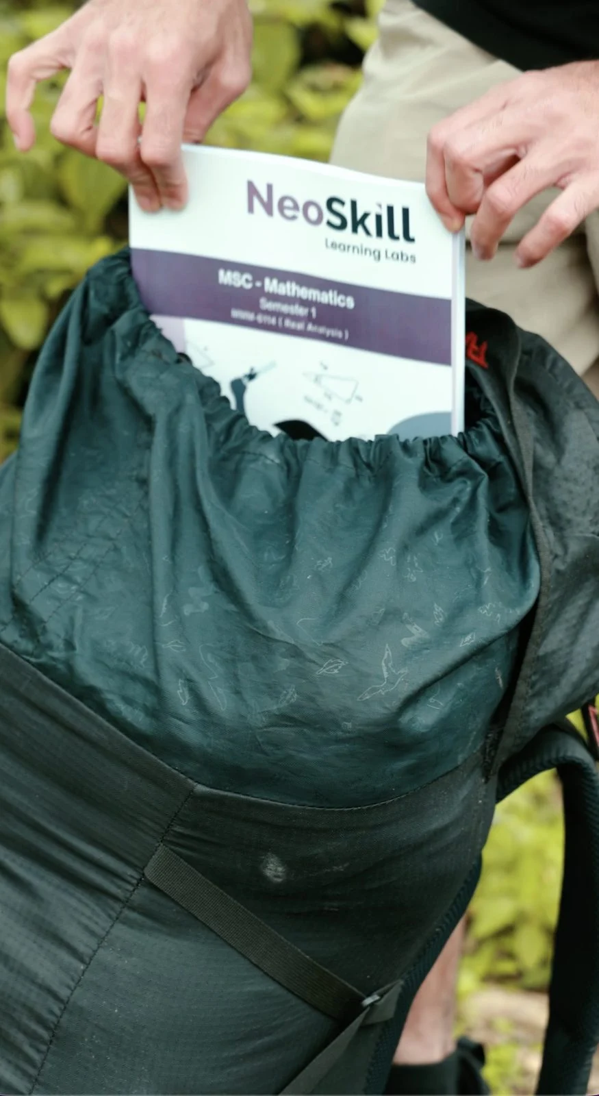 A printed NeoSkill MSc Mathematics study book being packed into a backpack